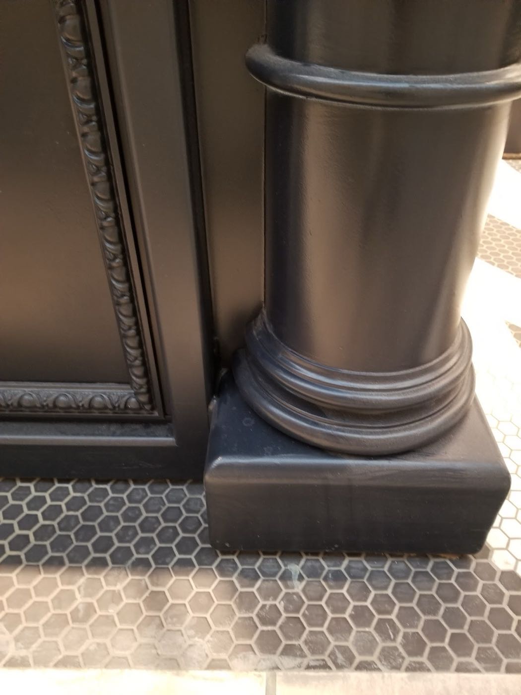 Black enamel storefront column with detailed molding on a hexagon tile floor