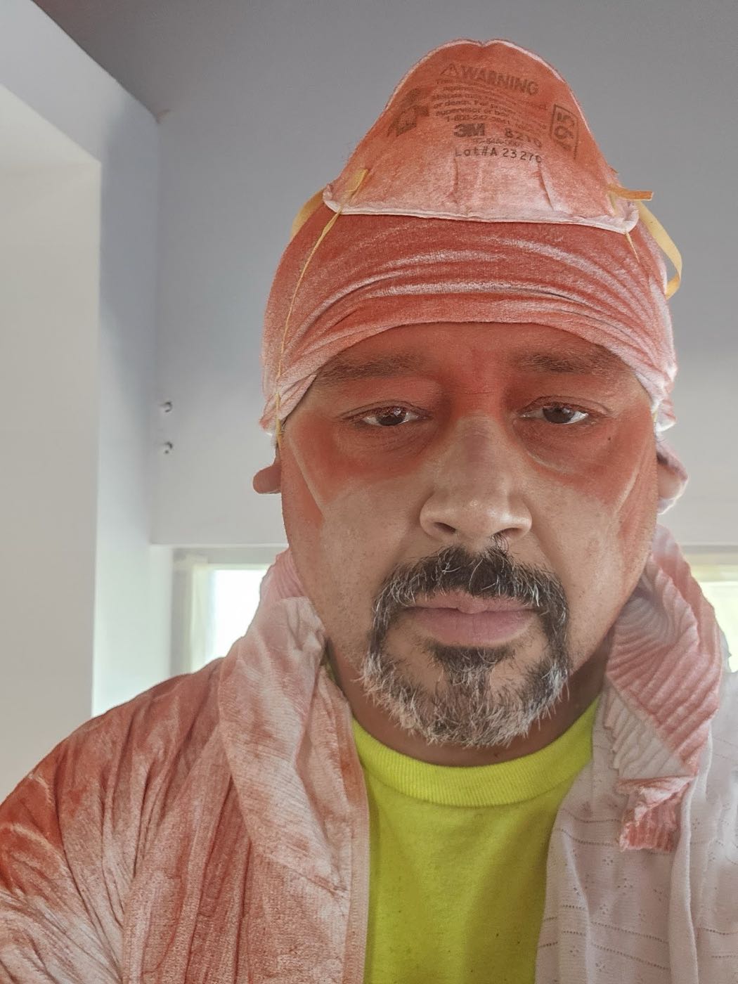 Juan Mario Hernandez covered in red paint overspray after a spray job, mask still on his head