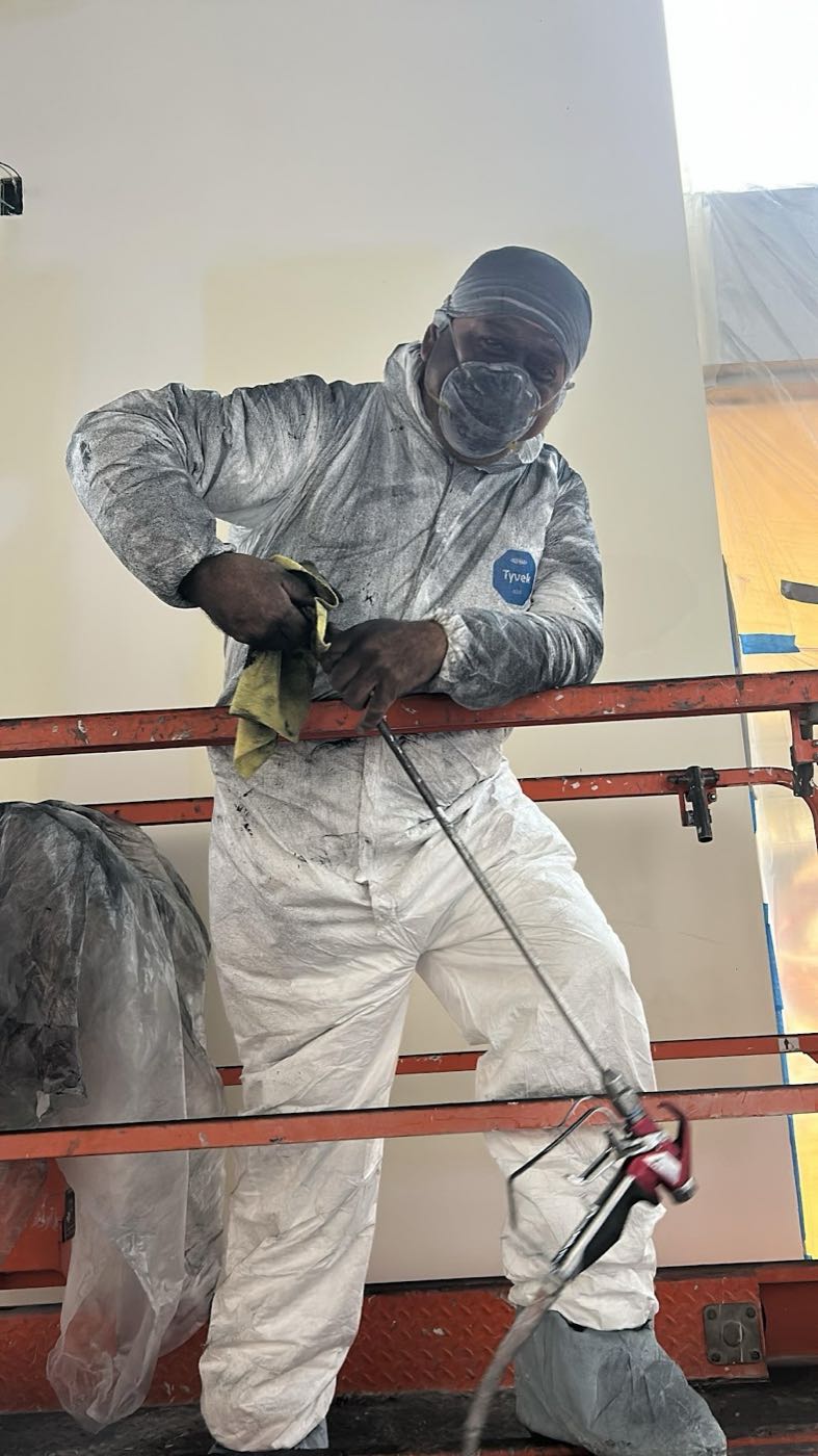 Juan Mario in a white spray suit on a lift, spraying a high ceiling